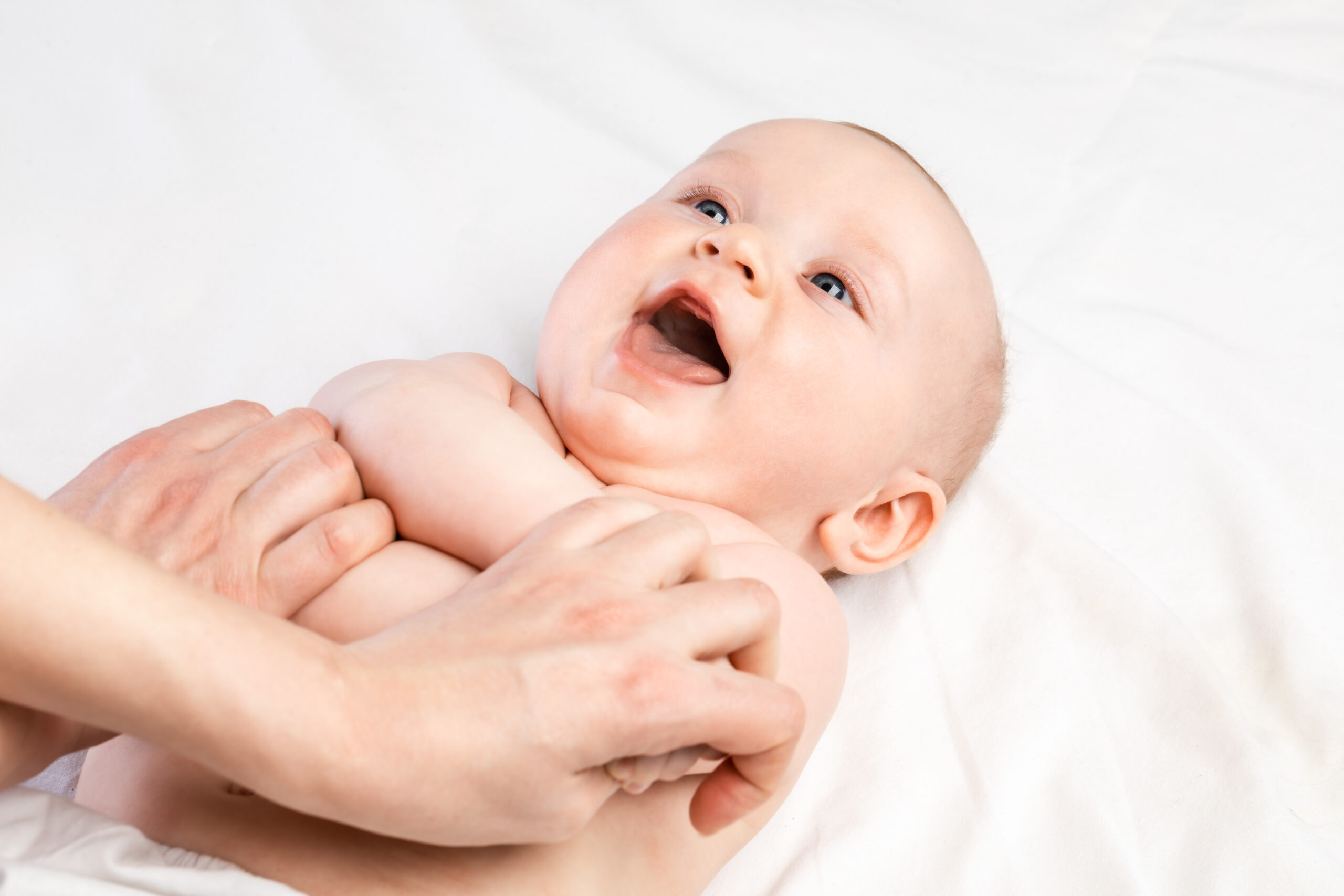 Happy 5-month baby boy receiving massage therapy in pediatric clinic. Manual therapist manipulates childs’s arms